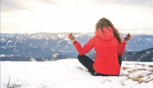 Woman sitting in a yoga pose on a wintery hilltop